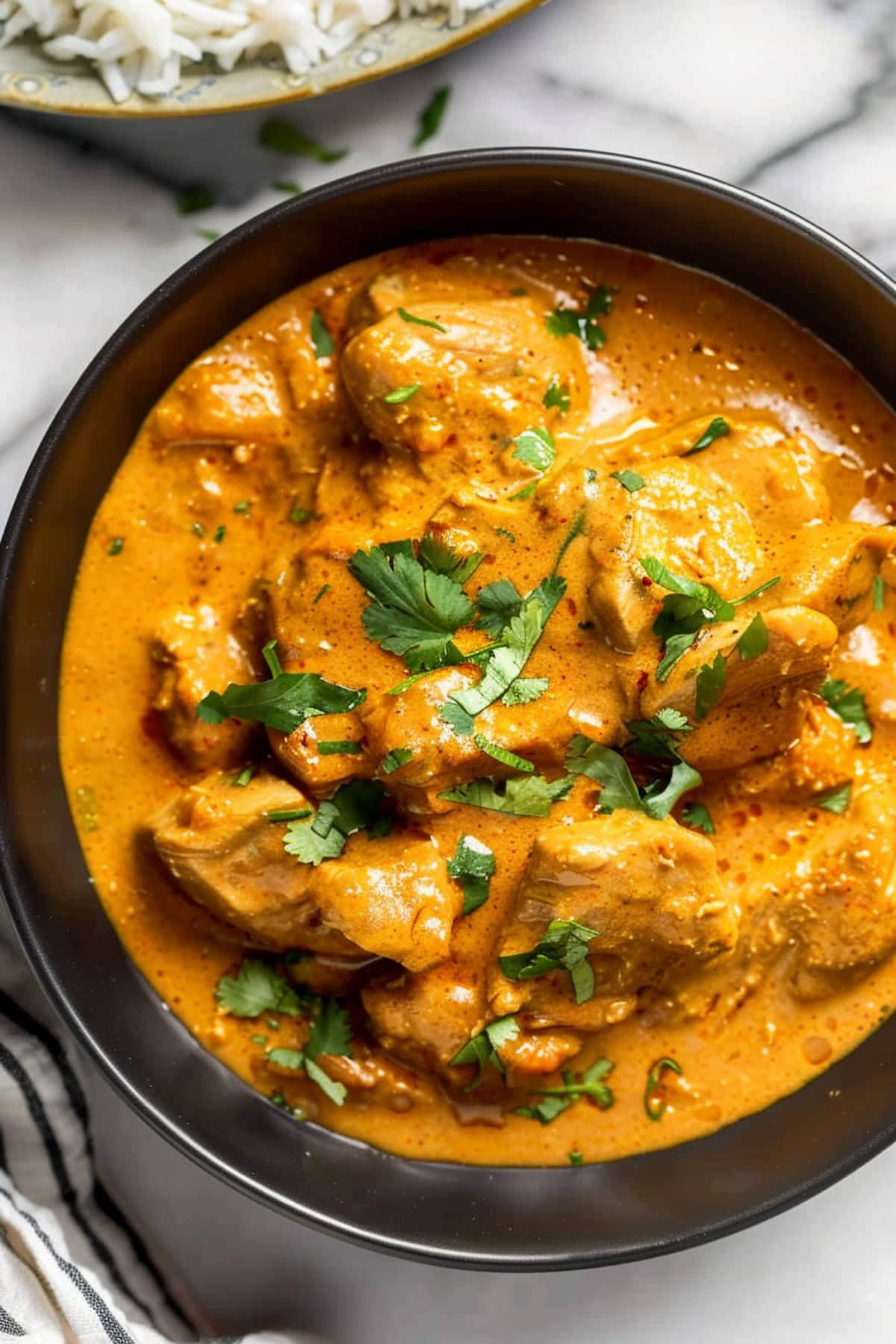 Homemade creamy coconut chicken curry garnished with cilantro in a black bowl, top down view.