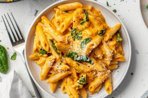 Creamy pumpkin pasta with spinach served in a white plate, fork on the side.