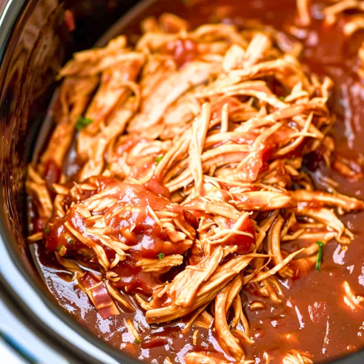 Closeup of shredded chicken with BBQ sauce in a slow cooker.