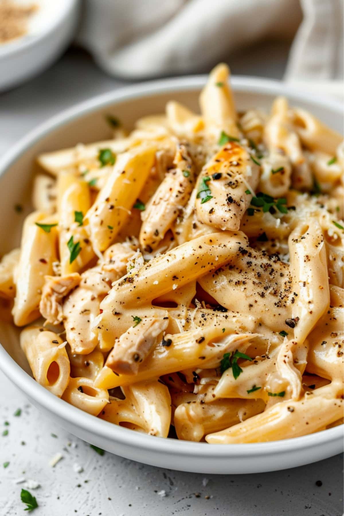 Penne pasta in Olive Garden sauce served in a white plate with grated parmesan cheese garnish.