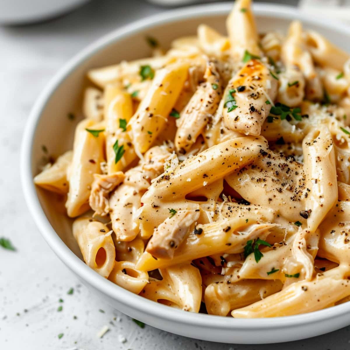 Crockpot cooked penne pasta with Olive Garden sauce and shredded chicken served on a white plate.