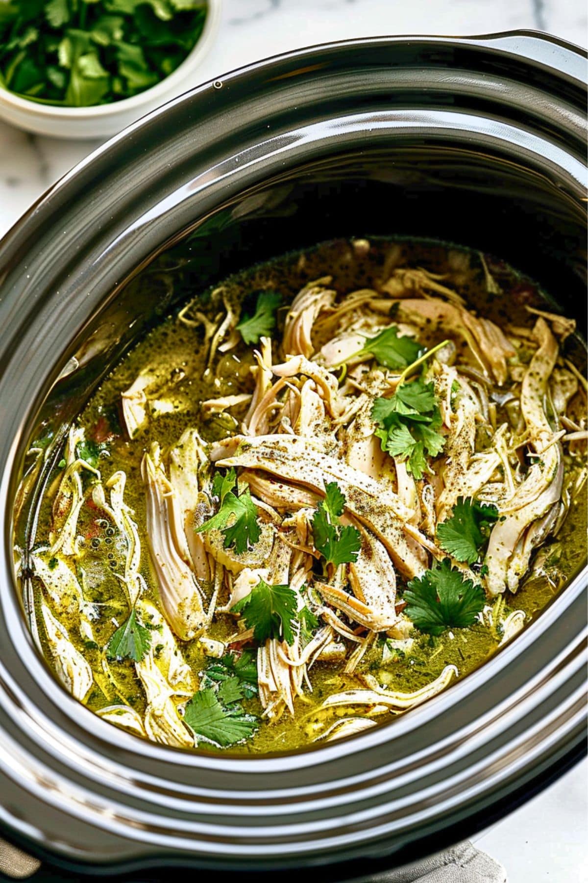 Shredded chicken cooked in verde salsa in a slow cooker.