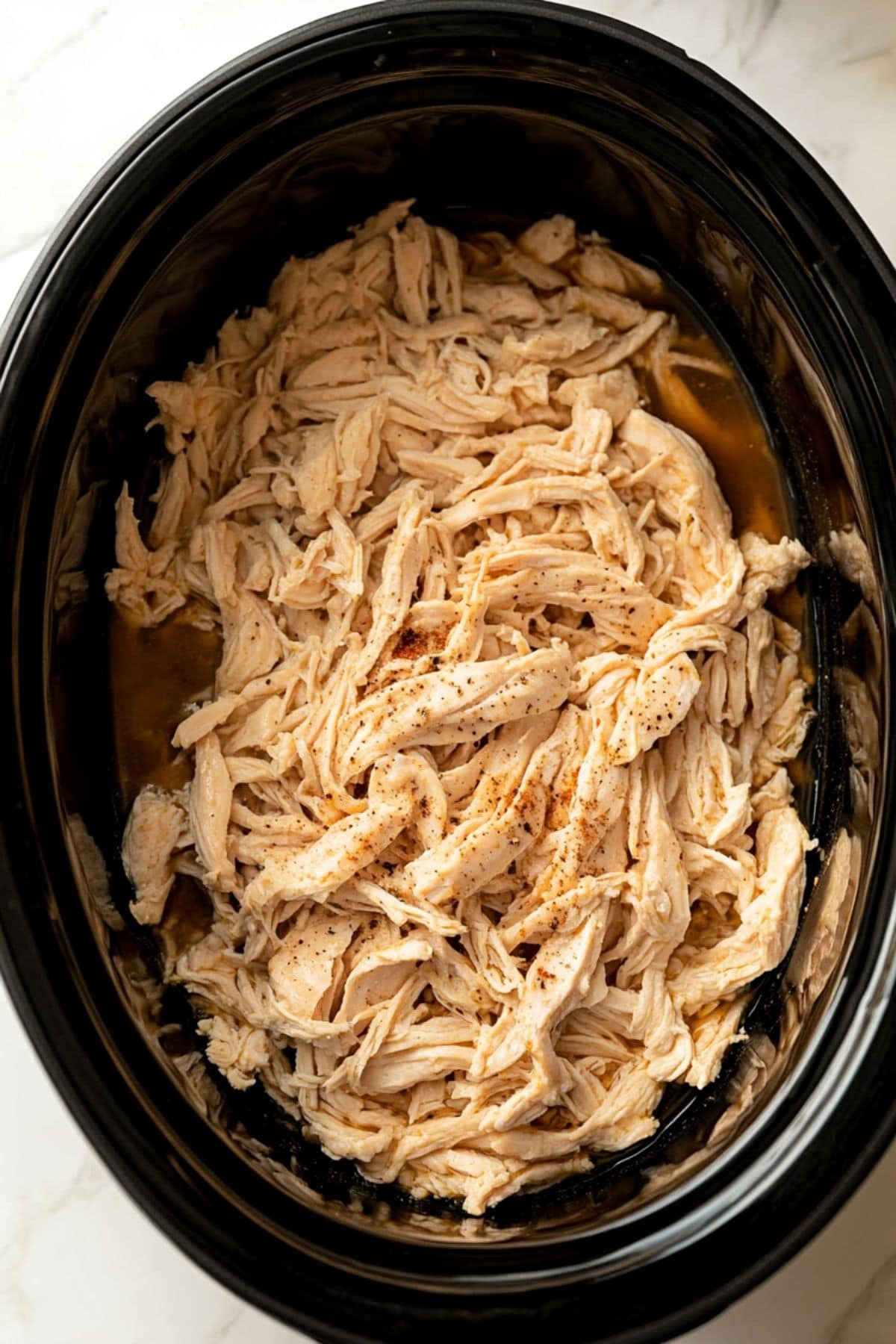 Shredded chicken with juices cooked inside slow cooker.