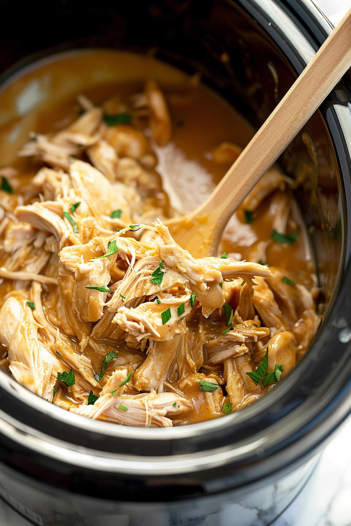 Shredded chicken with gravy inside a slow cooker.