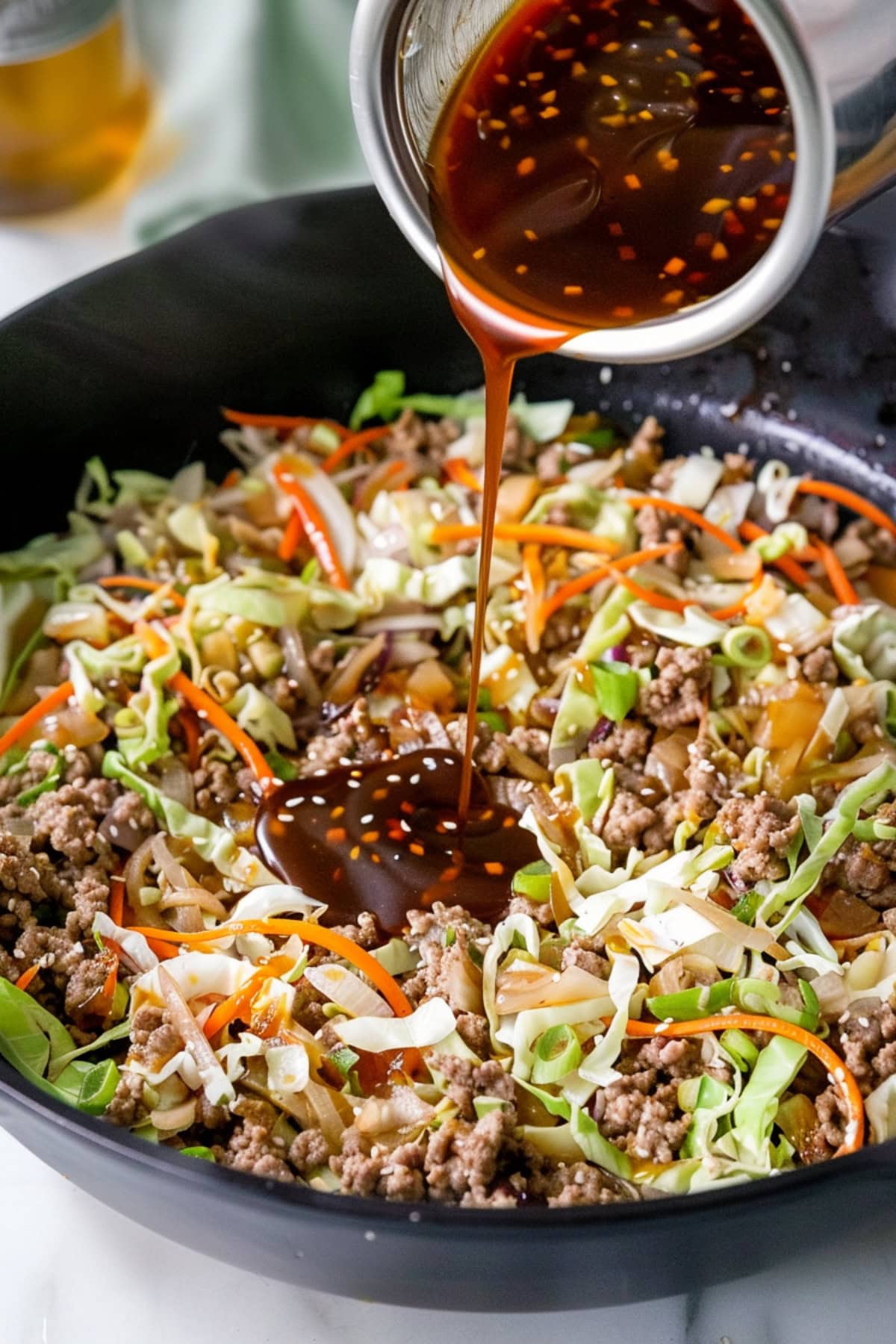 Pouring Hoisin Sauce into a Mix of Ground Beef, Cabbage and Carrots