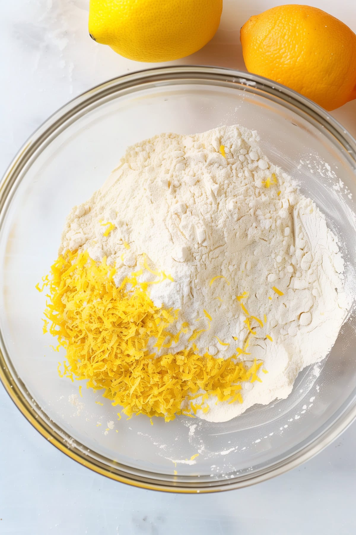 A glass bowl filled with flour and lemon zest, top view