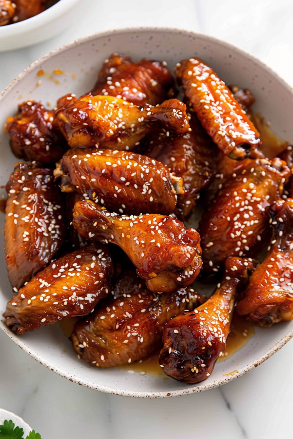 Saucy homemade honey garlic chicken wings with sesame seeds in a white bowl.