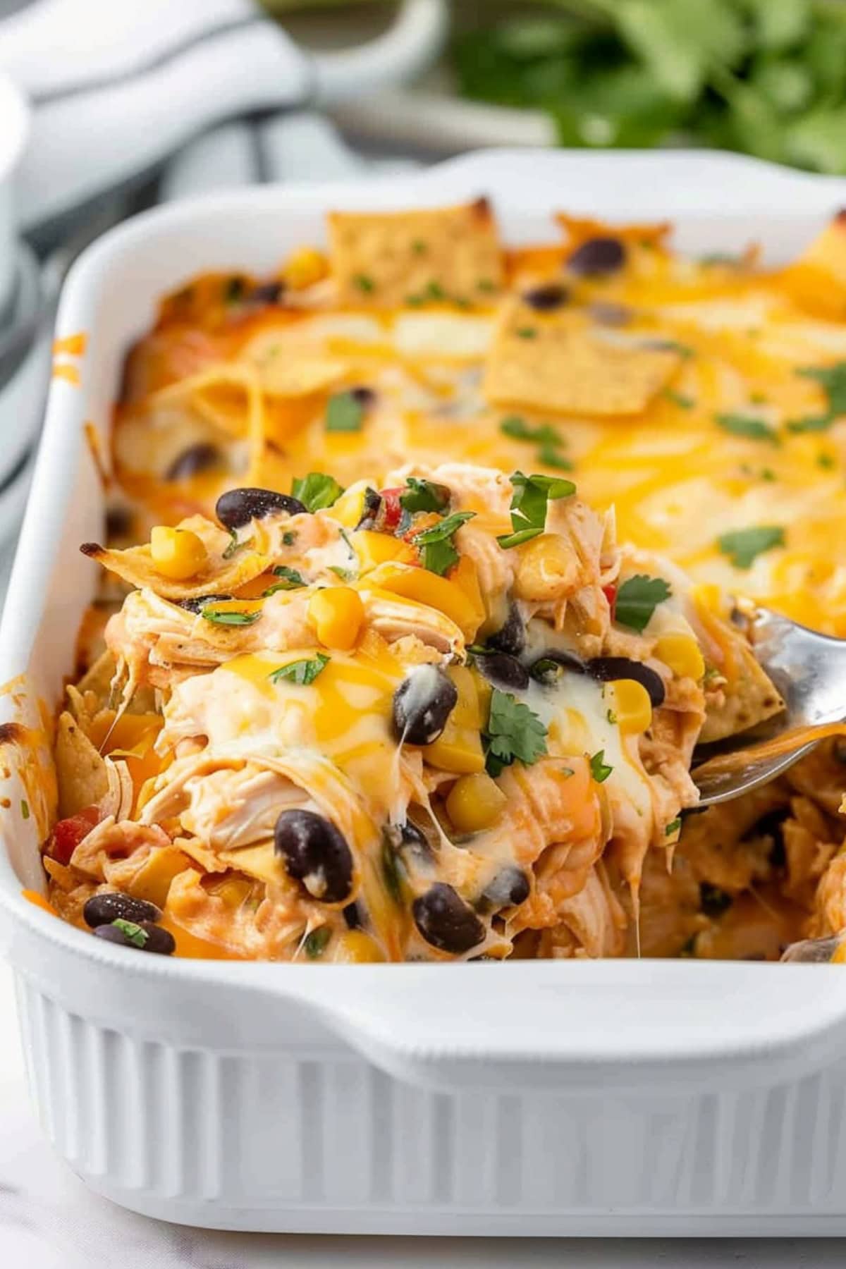 Serving spoon scooping a portion of Mexican chicken casserole in a baking dish.