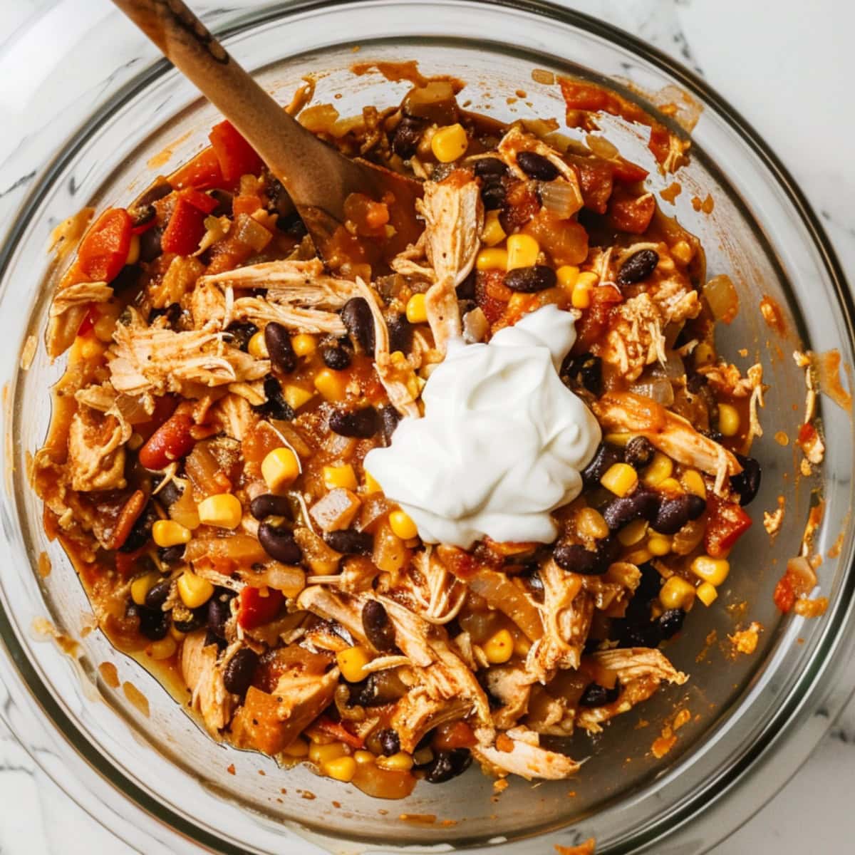 Cooked onion mixture, shredded chicken, black beans, corn, salt, chili powder, cumin, black pepper, fire-roasted tomatoes, cream of chicken soup, and sour cream in a clear bowl.