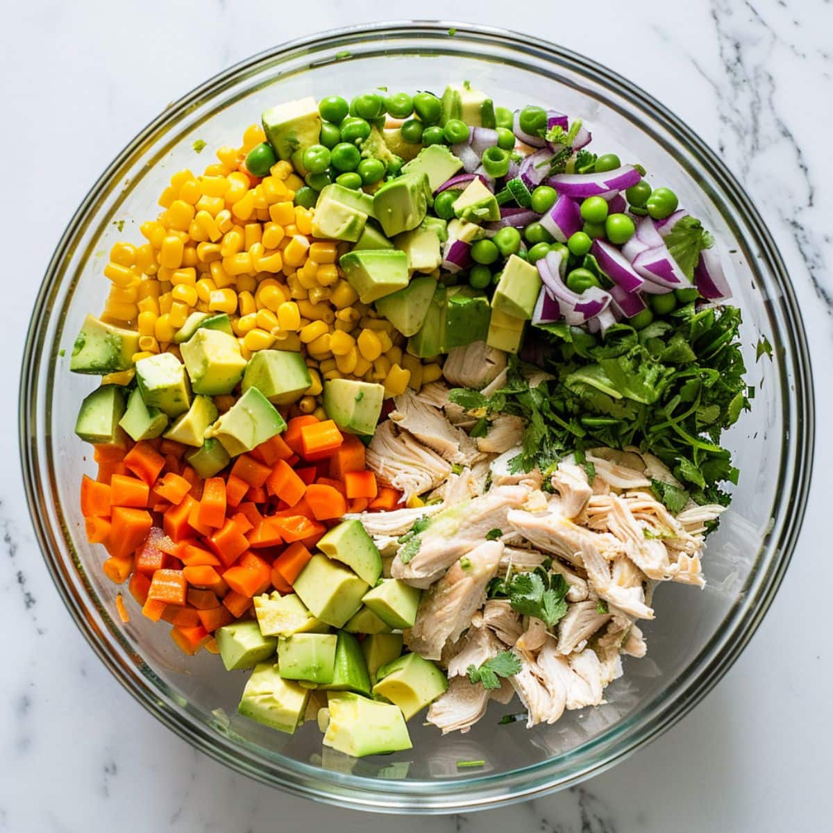 Shredded chicken, diced potatoes, mixed vegetables, diced avocado, red onion, chopped cilantro and thinly sliced green onions in a large glass mixing bowl, top down view