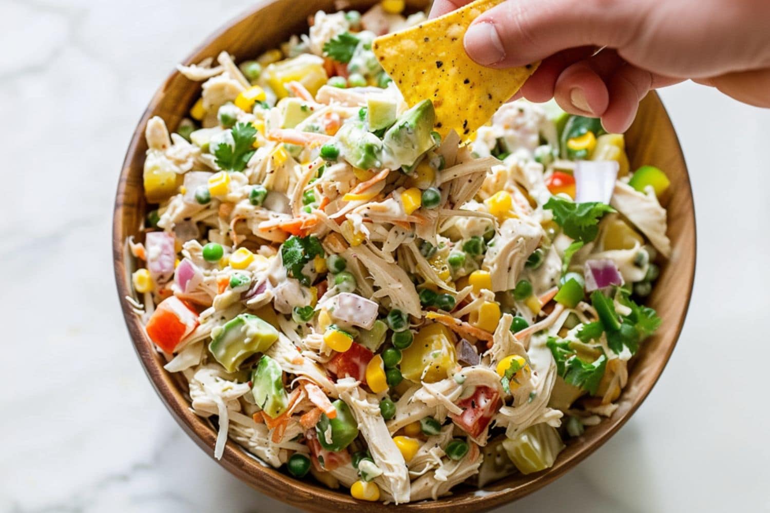 Tortilla dipped in a serving of Mexican chicken salad in a wooden bowl.