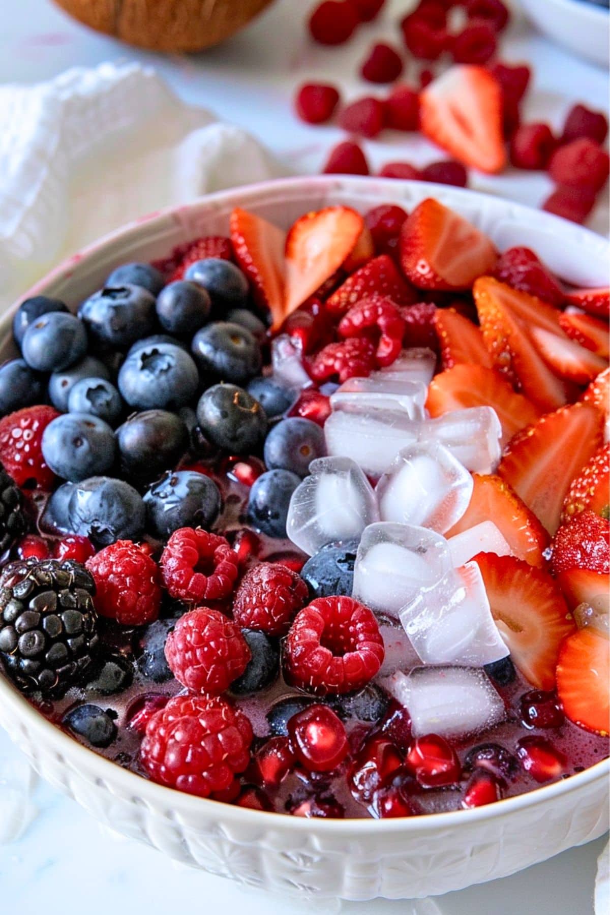 Blueberries, blackberries, raspberries, pomegranate seeds, and chopped strawberries in a medium-sized bowl with cube ice and coconut water.
