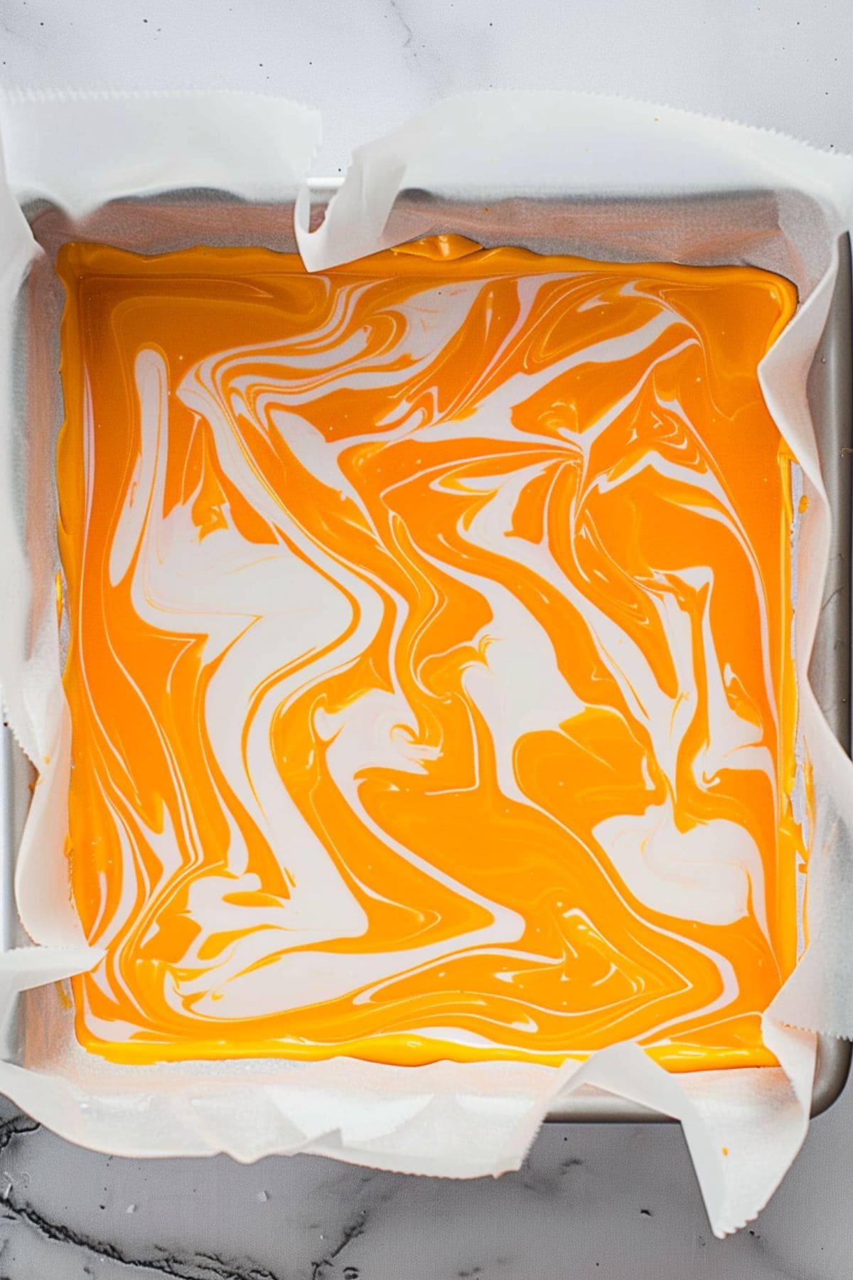 Marbled orange creamsicle fudge in a baking pan with parchment, top view