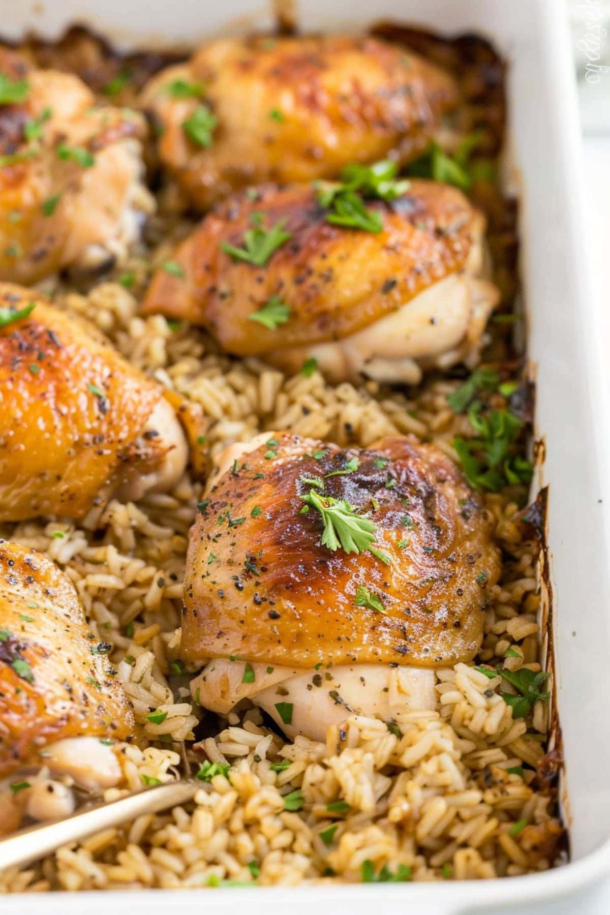 Chicken baked on top of seasoned rice in a rectangular white baking dish