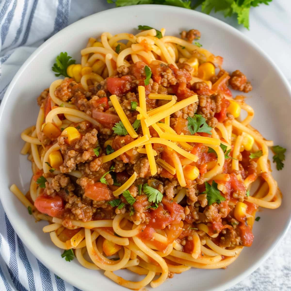 Mexican spaghetti with ground beef, topped with shredded cheese in a white plate.