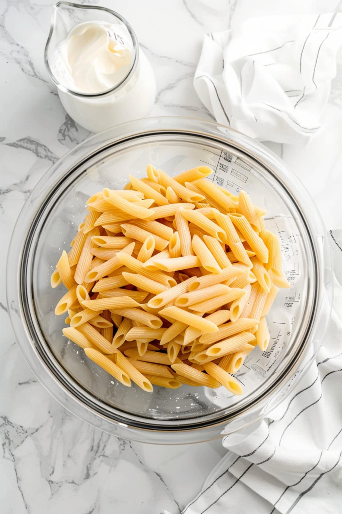 Raw penne pasta in a clear bowl.