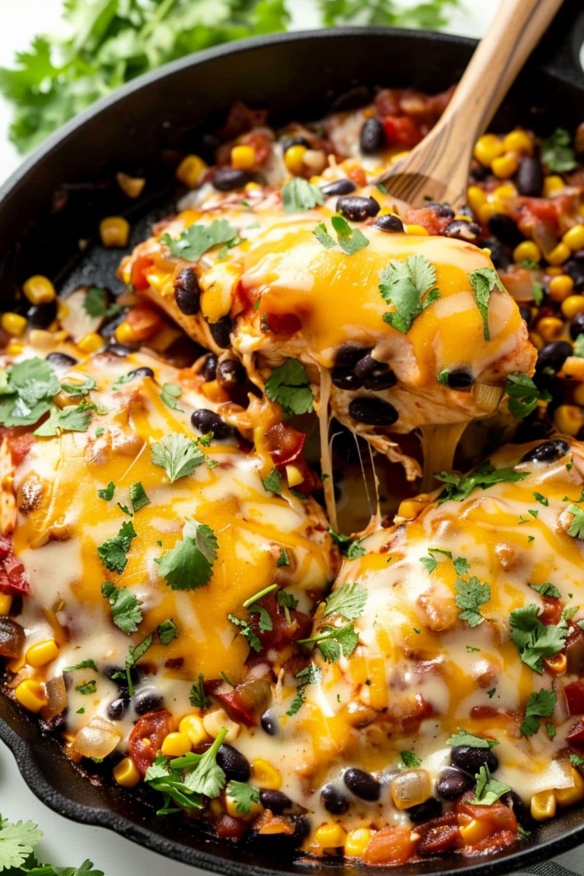 Wooden spoon lifting a cheesy serving of Santa Fe chicken with corn, black beans and diced tomatoes.