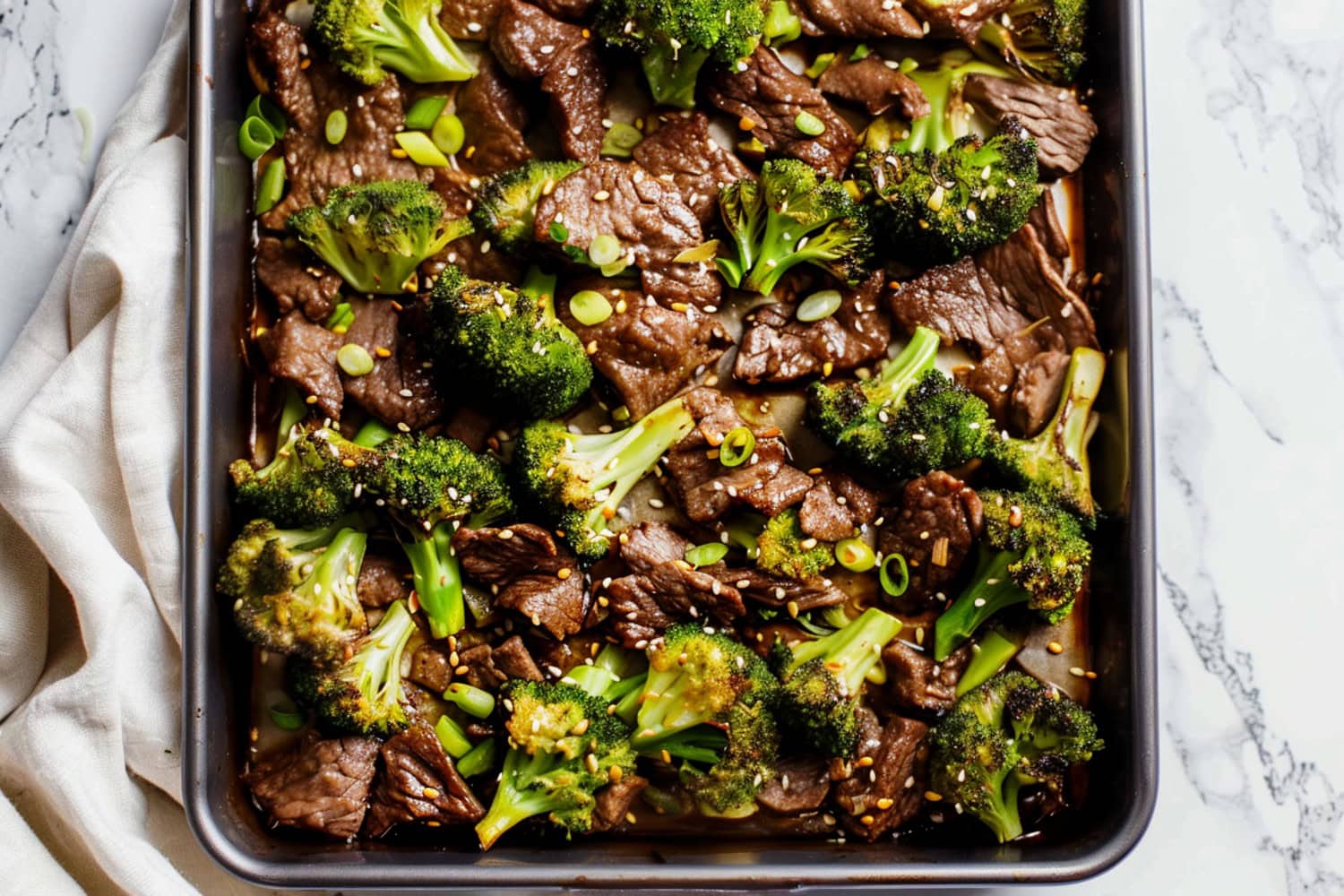 Top view of sheet pan beef and broccoli on a white marble table.