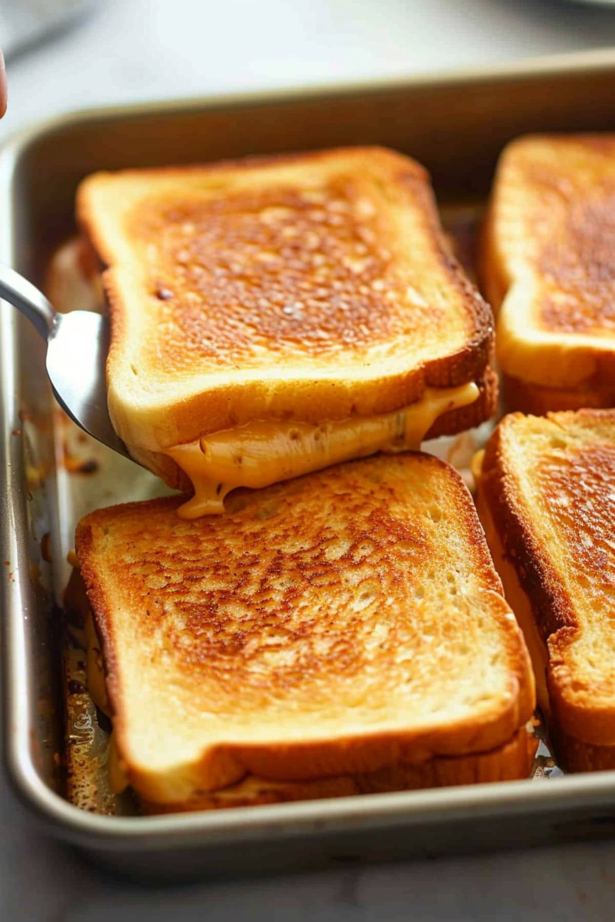 Grilled cheese sandwich in a sheet pan lifted by a ladle.