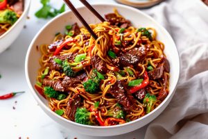 Sticky beef noodles served in a white bowl, chopstick lifting the noodles.