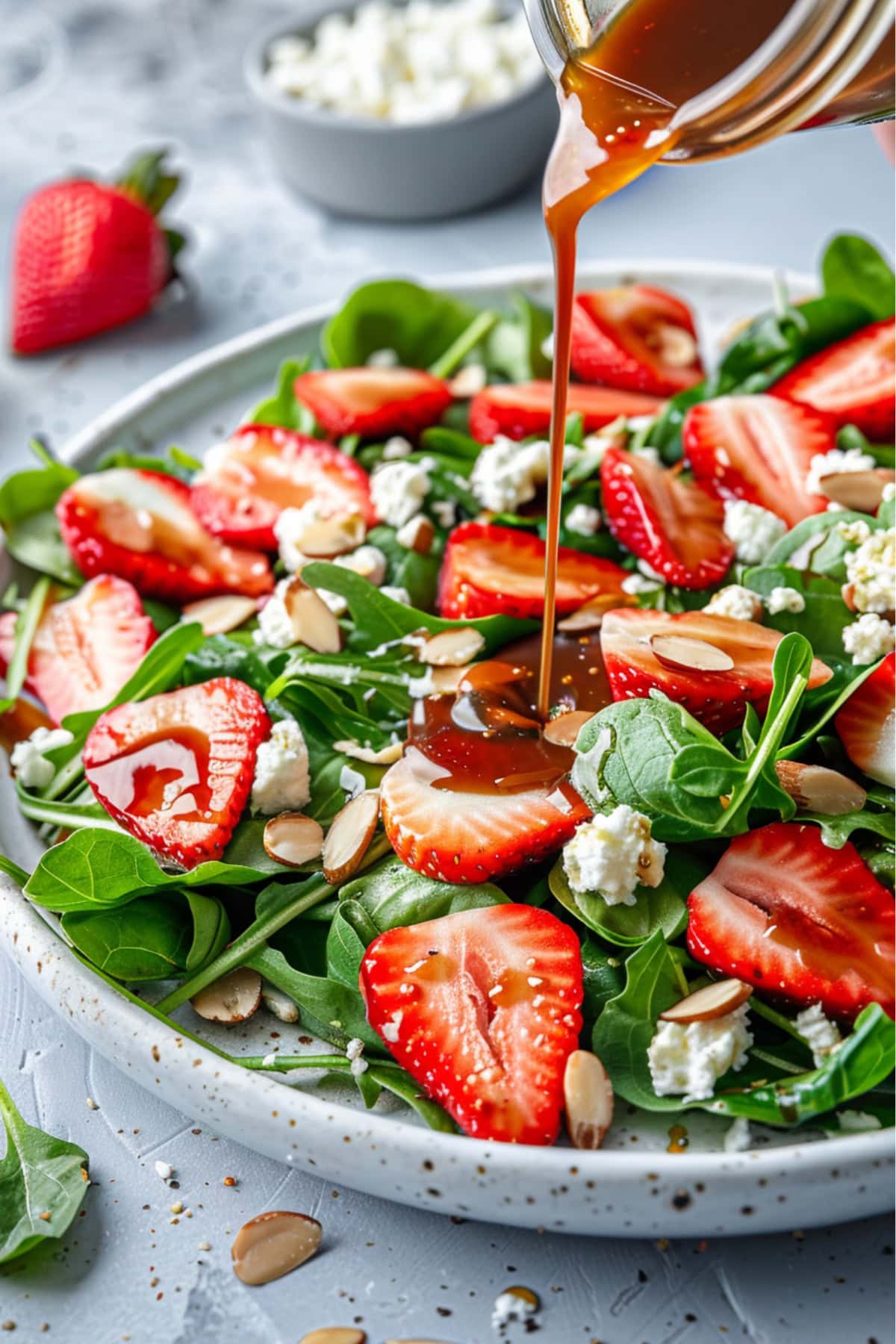 Balsamic dressing drizzling over strawberry salad in a white plate.