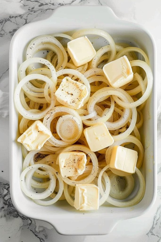 Sliced onion rings in a baking dish topped with butter cubes.