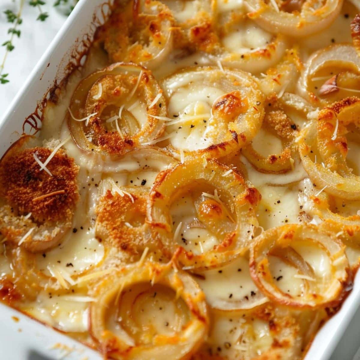 Baked onions with melted cheese and butter in a rectangle baking dish.