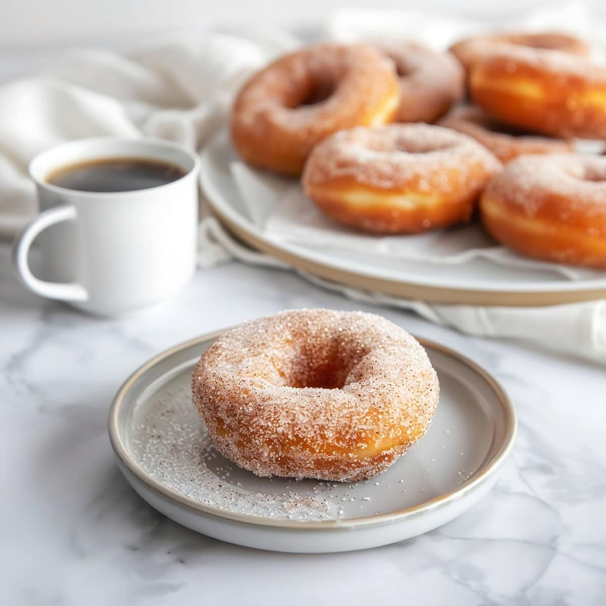 Cinnamon sugar donut on a plate with a cup of coffee and a bigger plate of donuts in the background