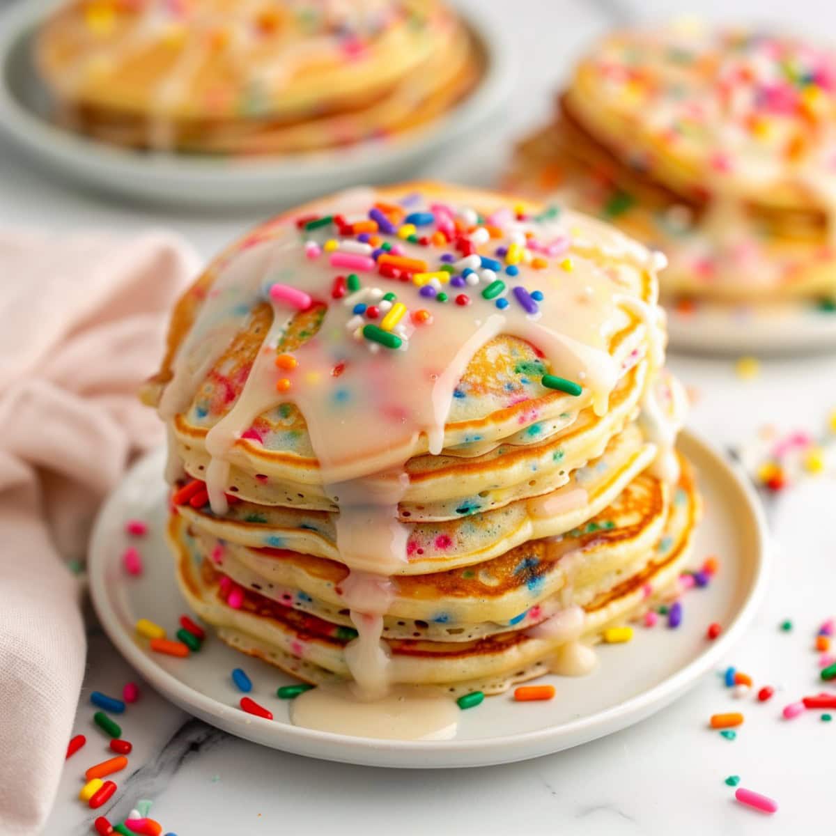 Funfetti pancakes served on plate drizzled with white glaze and sprinkles.