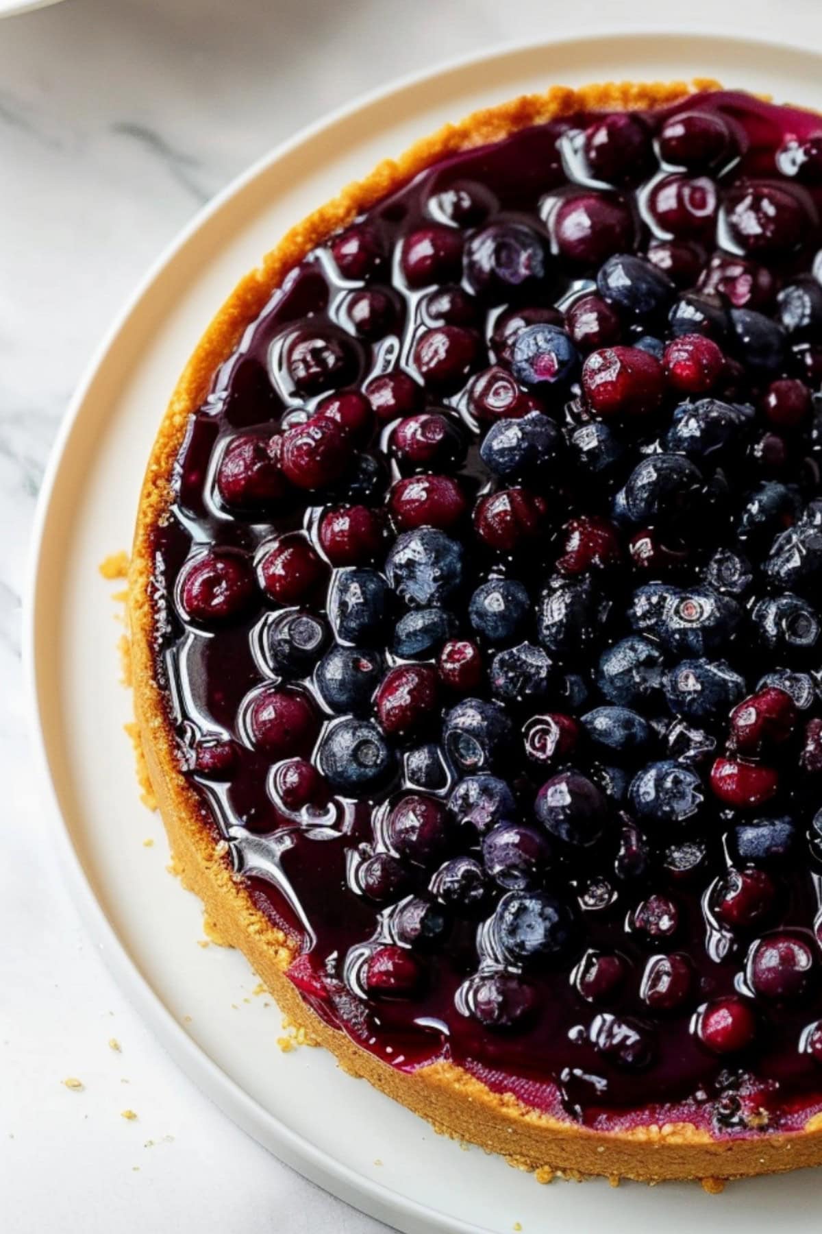 A whole lemon blueberry cheesecake on a white serving plate, top down view.