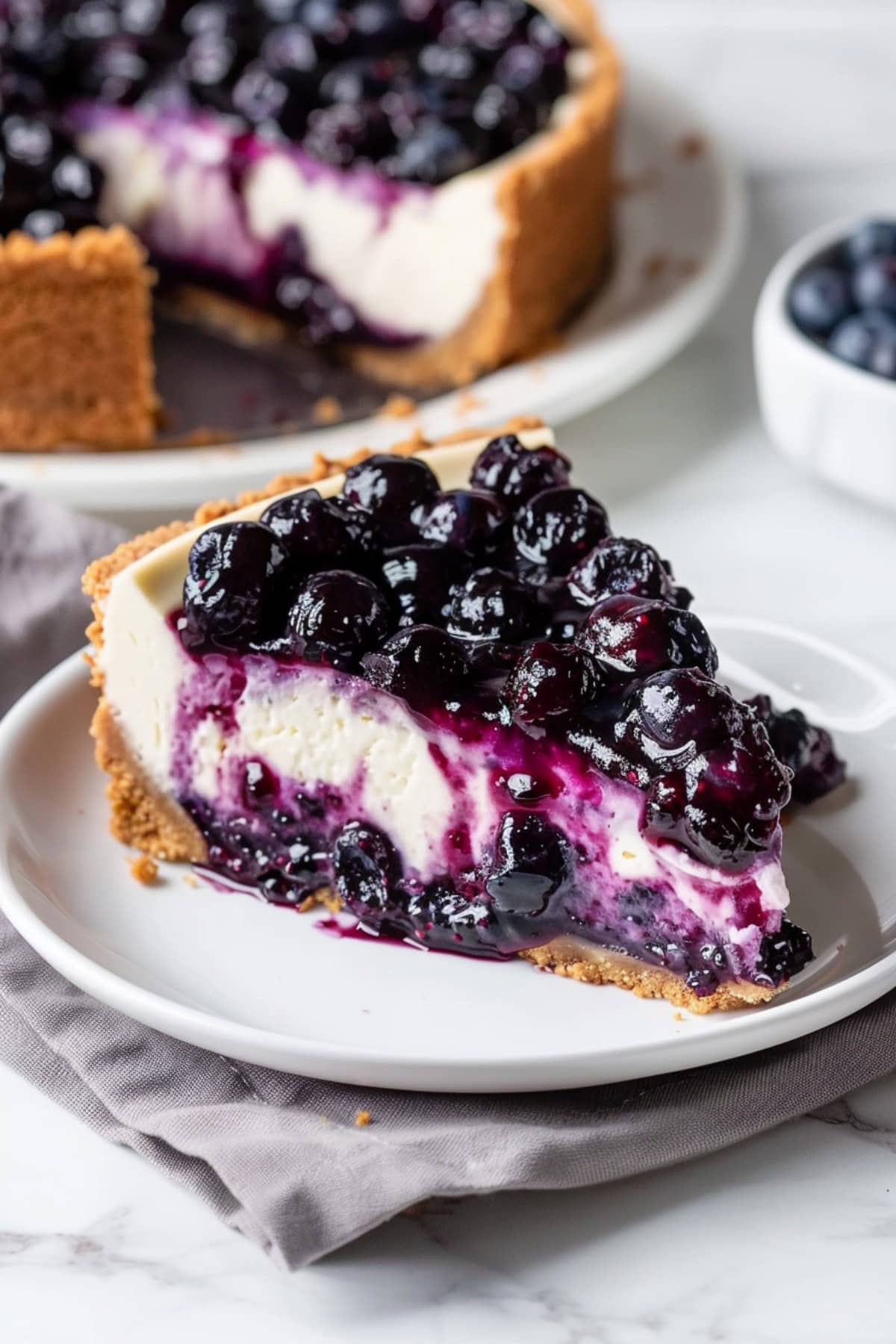 Lemon blueberry cheesecake slice served on a white plate with blueberry compote on top