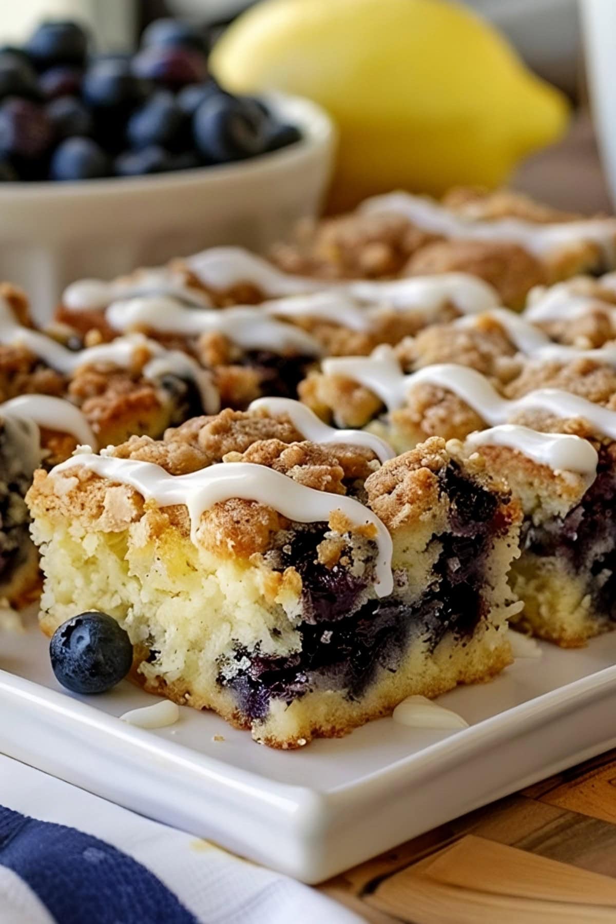 Lemon blueberry coffee cake sliced on a white serving plate with glaze drizzled on top