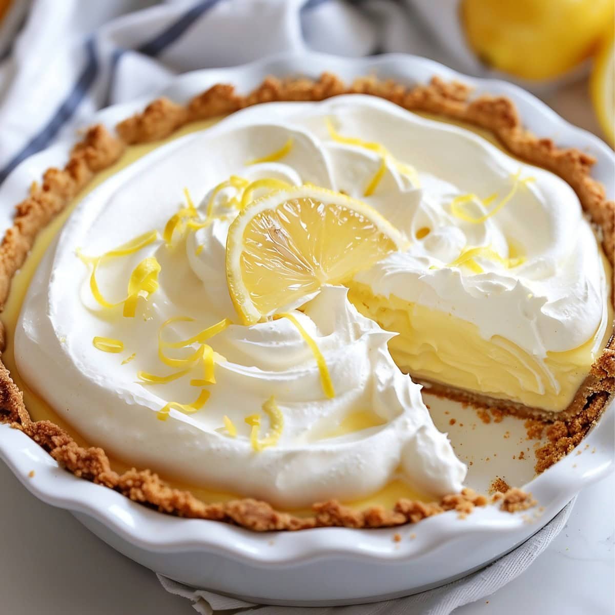 Lemon Cream Pie in a white baking dish garnished with lemon zest and lemon slice. 