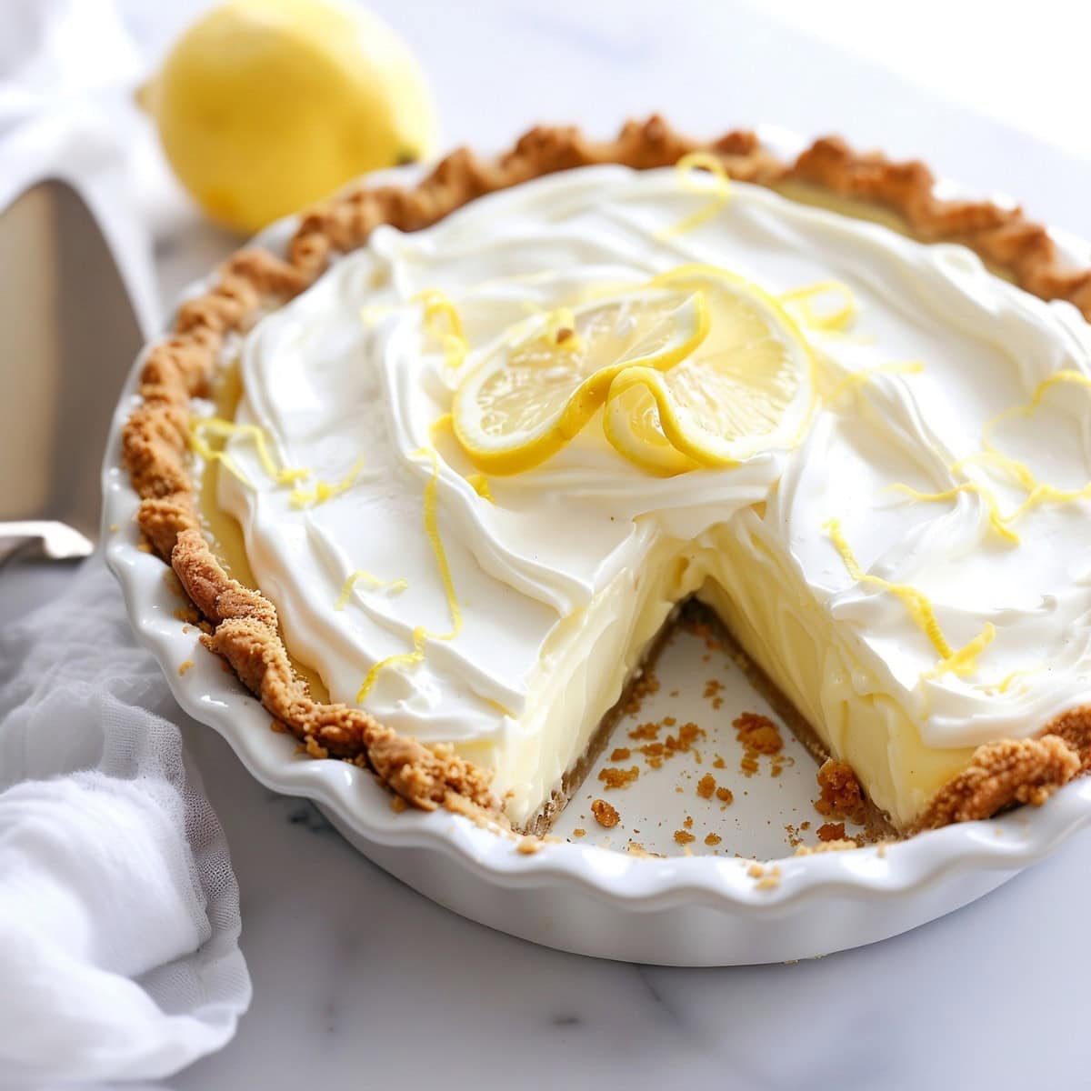 Lemon Cream Pie in a white pie dish slice missing. 