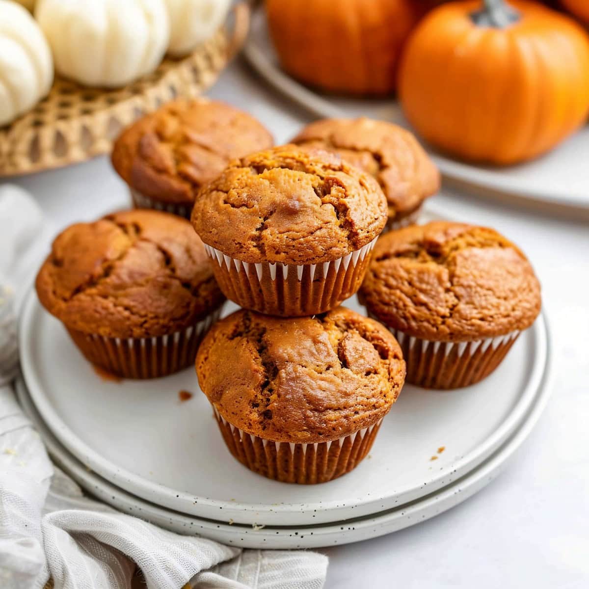 Pumpkin banana muffins on a plate with white and orange mini pumpkins in the background