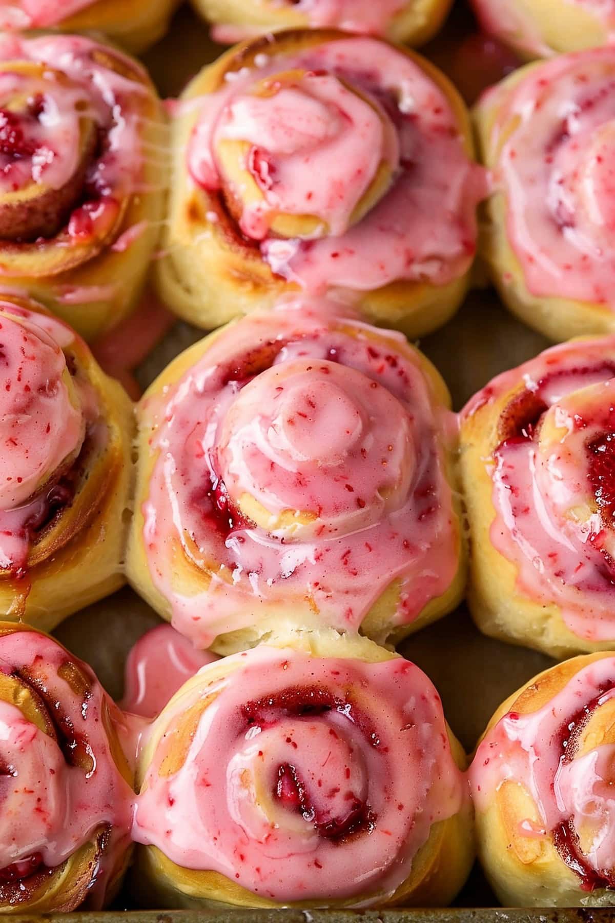 Soft and fluffy homemade strawberry cinnamon rolls with pink cream cheese glaze, close up