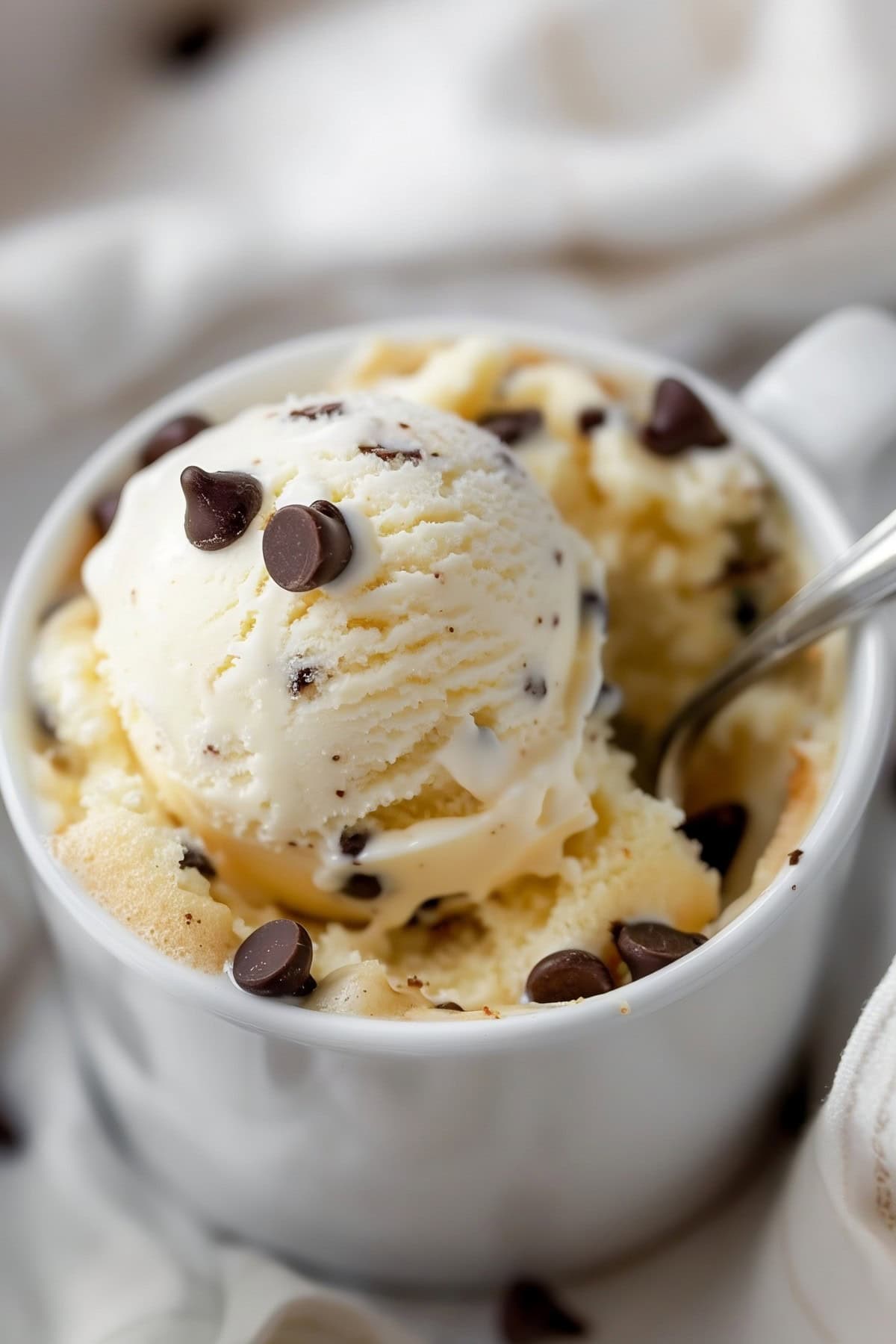 Vanilla Mug Cake topped with a scoop of vanilla ice cream and chocolate chips, with Spoon, Close-Up