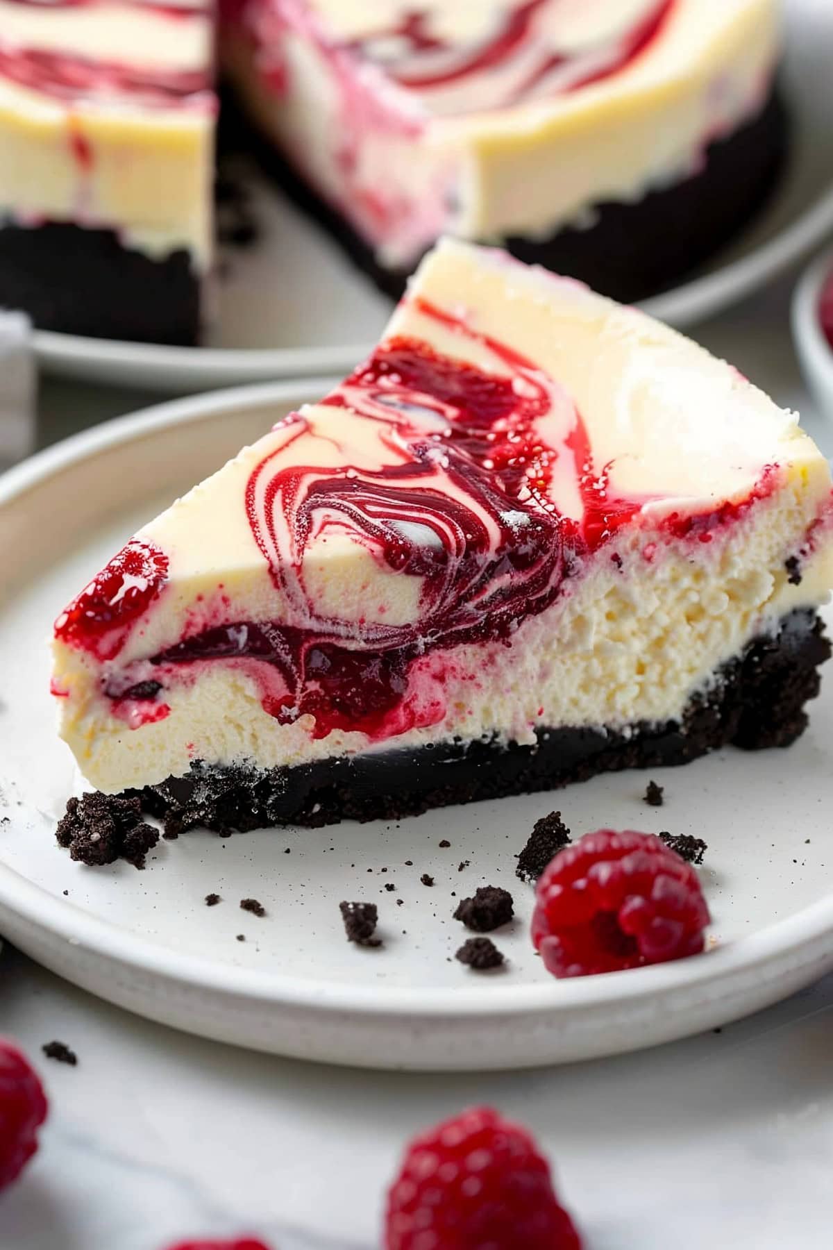 A slice of white chocolate raspberry cheesecake served on a white plate.