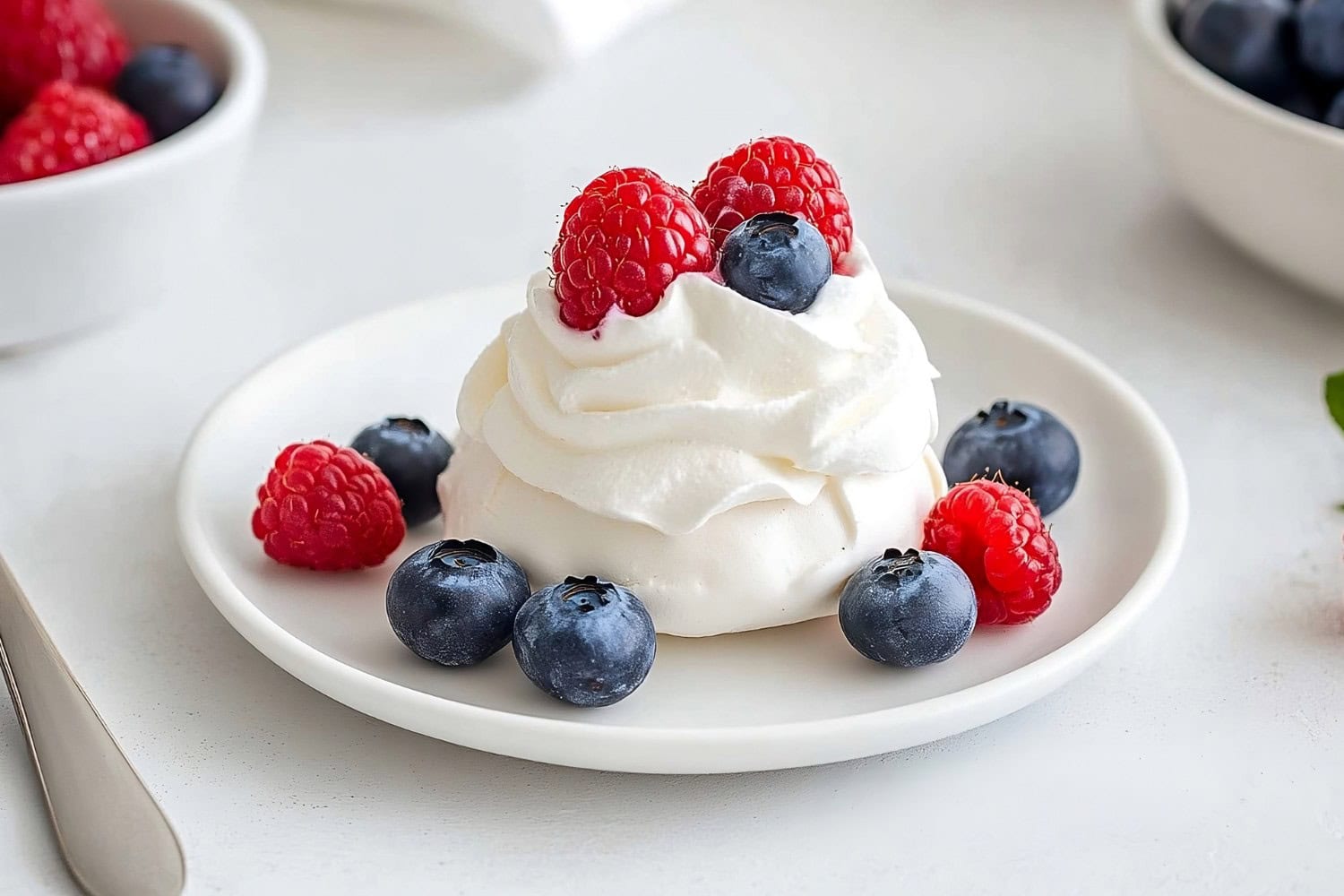 A single mini pavlova with a light, airy meringue base, topped with a rich layer of whipped cream and fresh berries.