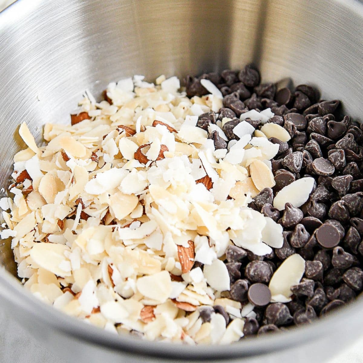 Chocolate chips, coconut flakes, chopped almonds in a large metal mixing bowl.