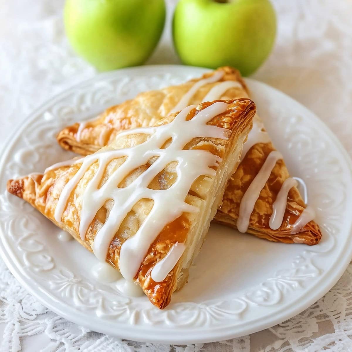 Two apple turnovers on a white plate with fresh green apples on the side