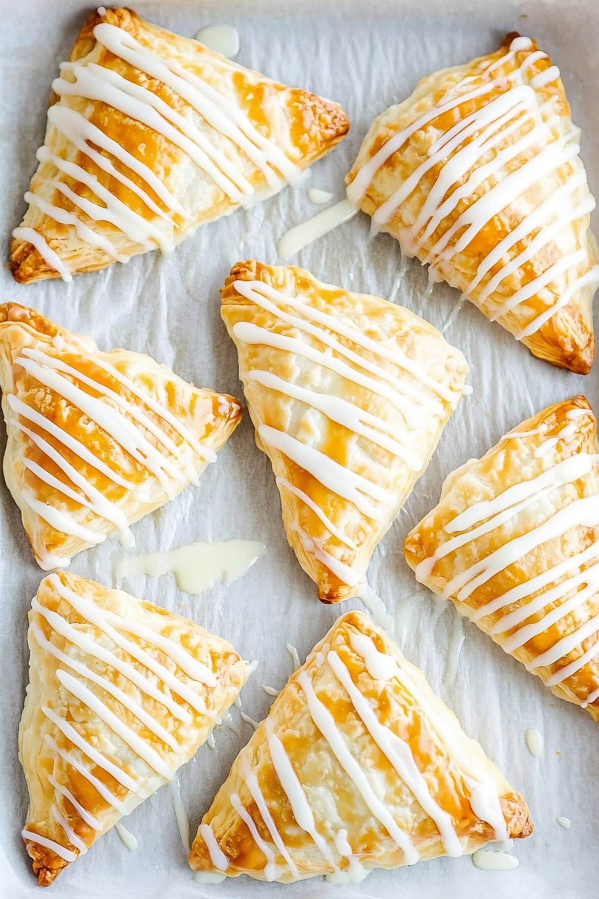 Homemade apple turnovers with vanilla glaze on parchment paper, top view