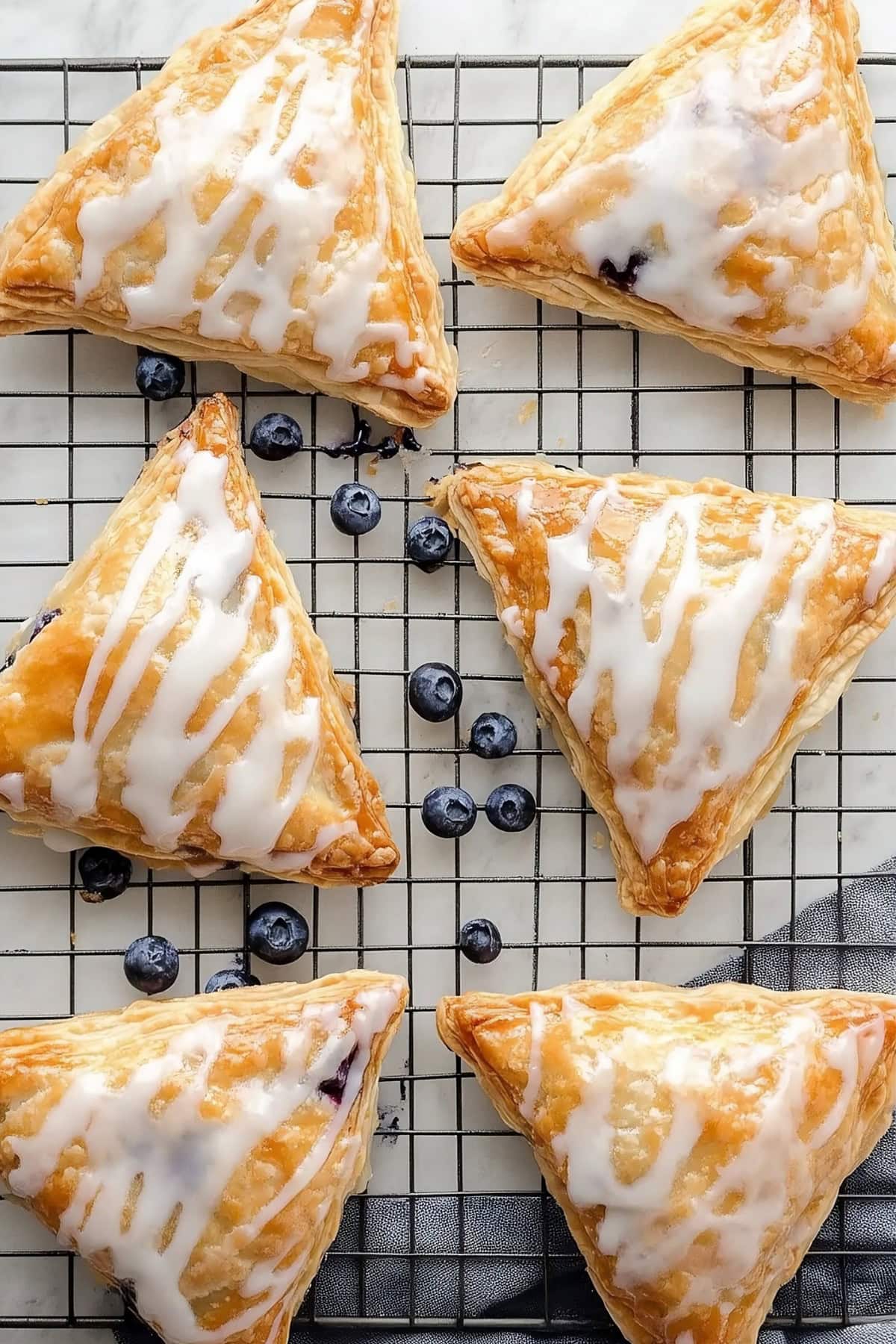 Overhead view of blueberry turnovers with sweet glaze on a cooling rack.