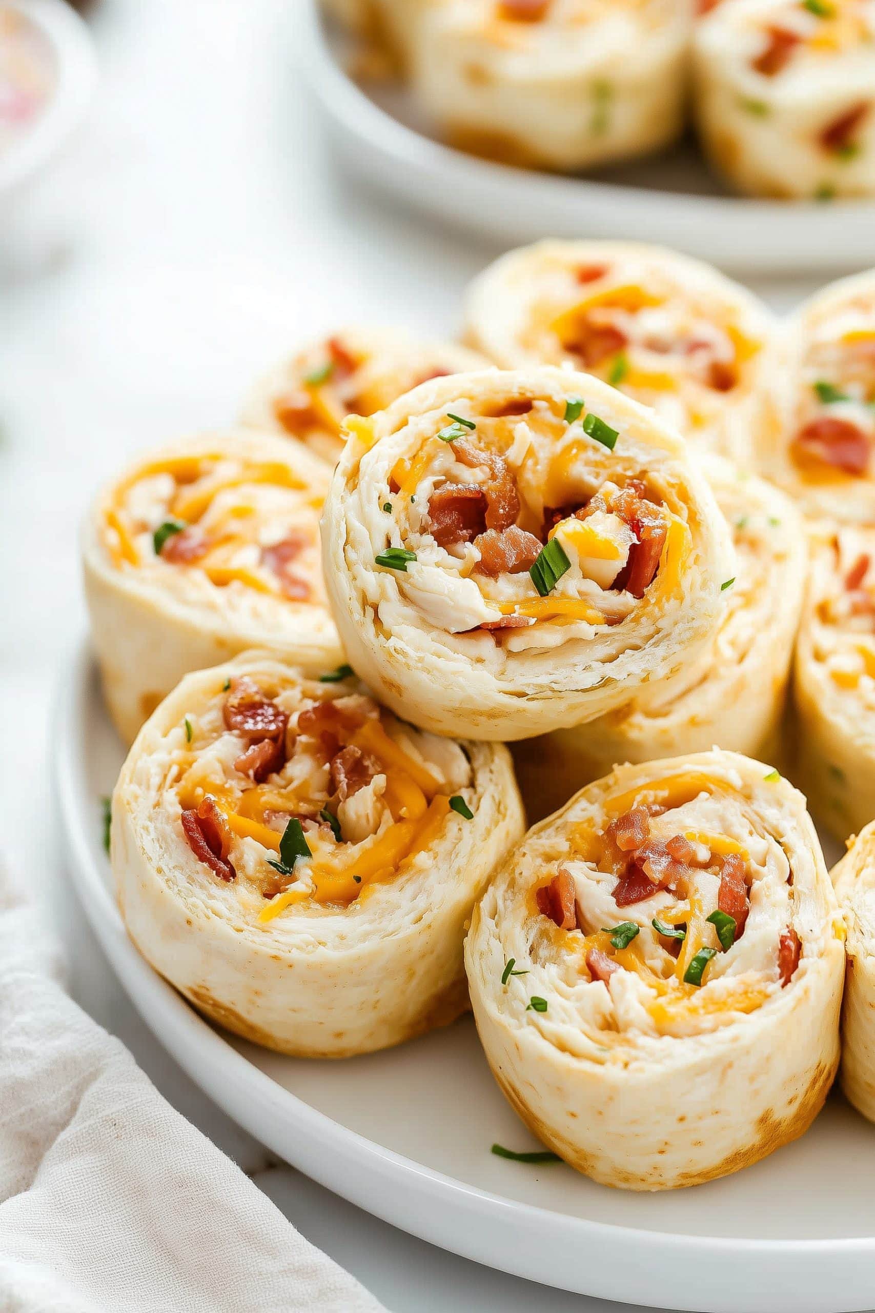 A stack of bacon ranch pinwheels with chopped chives and cheese.