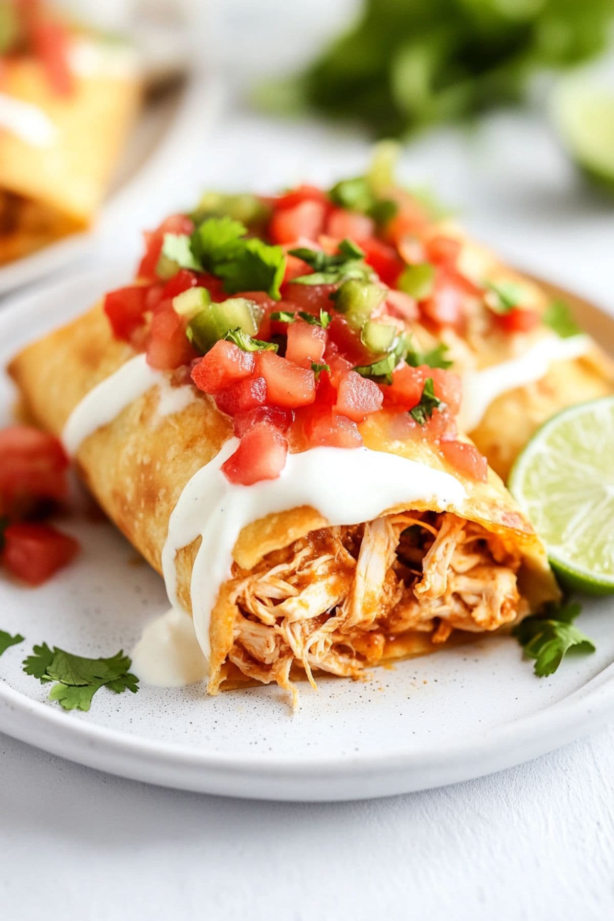 Chicken chimichanga cut in half with cheesy shredded chicken served on a white plate garnished with salsa and sour cream.