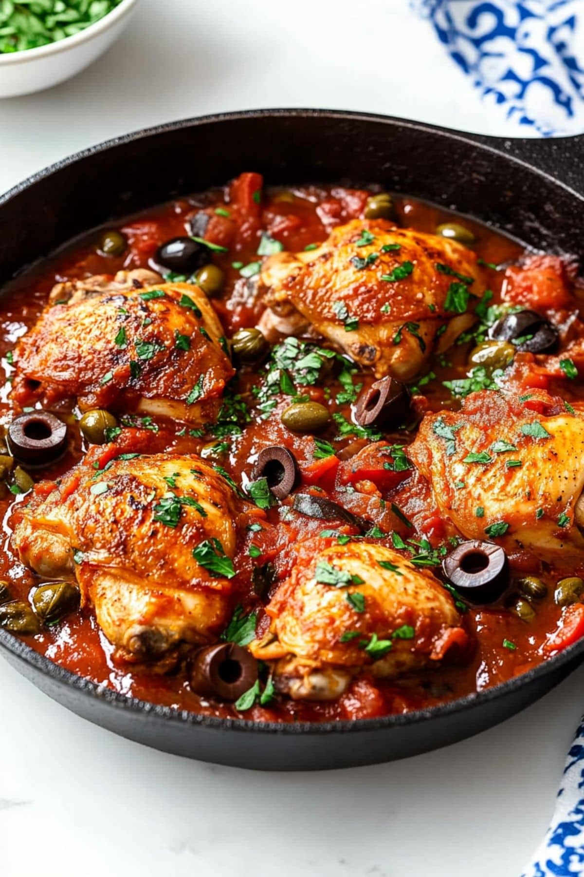 Chicken puttanesca made with chicken thigh, olives, capers, anchovies, and tomato sauce cooked in a cast iron skillet.