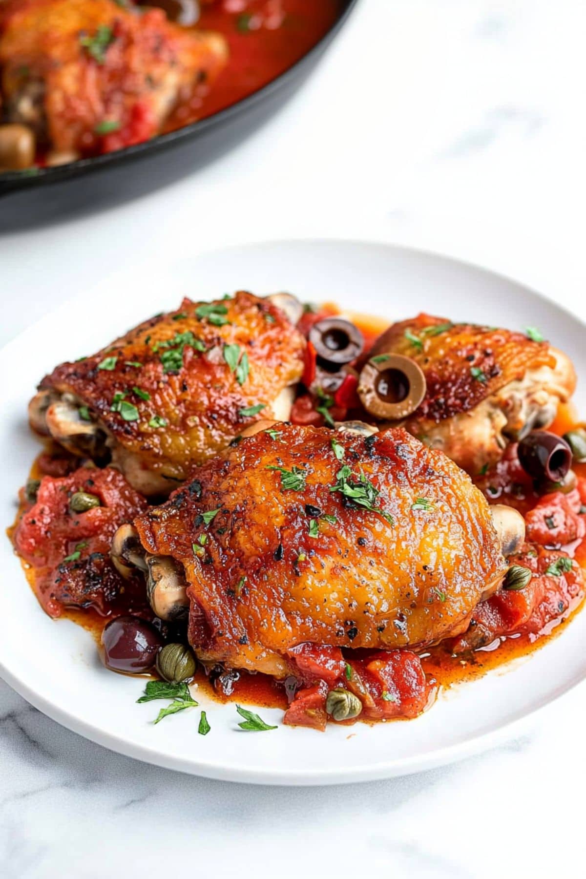 Chicken puttanesca served on a white plate.