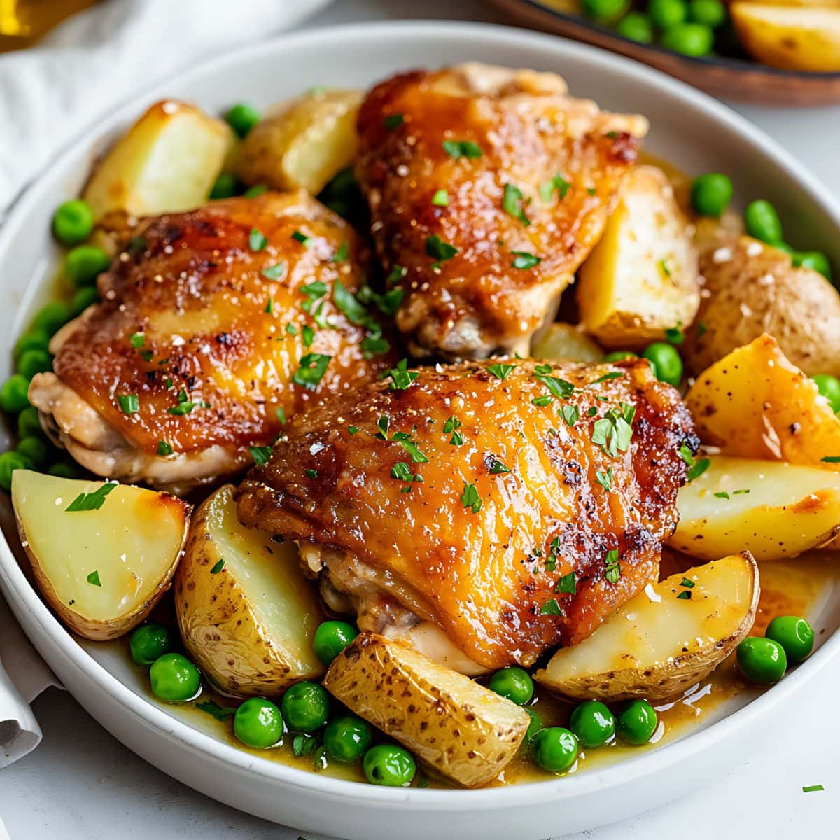 Chicago style Vesuvio featuring juicy thighs cooked with buttery sauce, green peas and potato wedges served in a white plate.