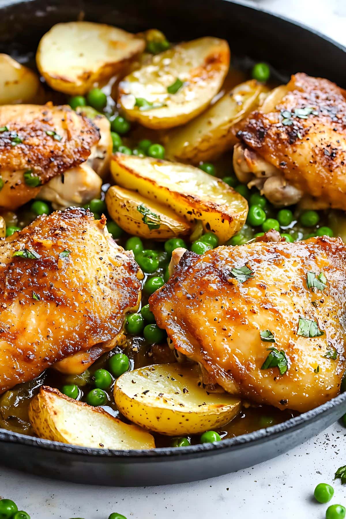 Chicken thigh with green peas and potato wedges soaked in lemony butter sauce cooked in a skillet pan, close up