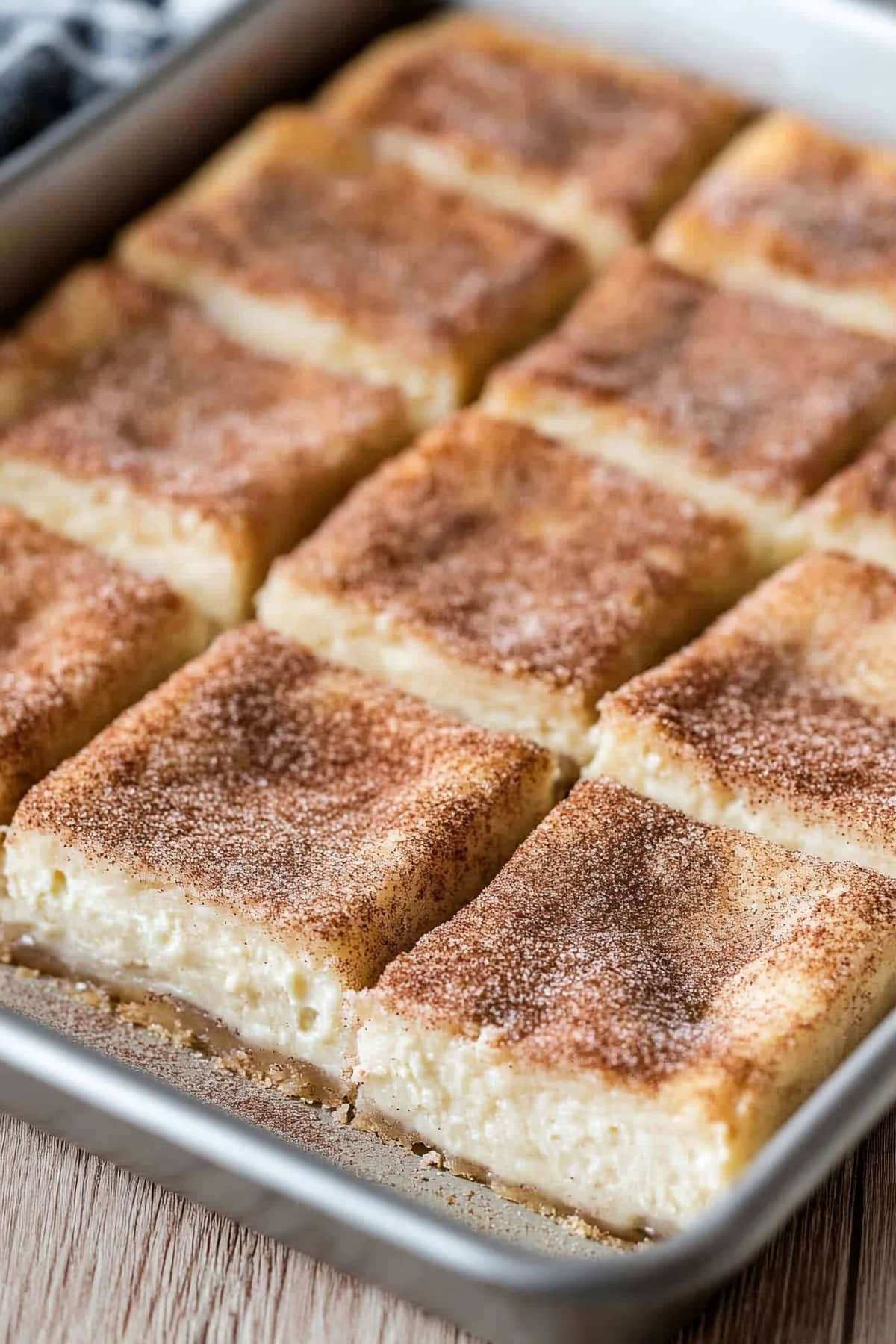 Homemade churro cheesecake bars with cinnamon sugar slice on a baking tray.